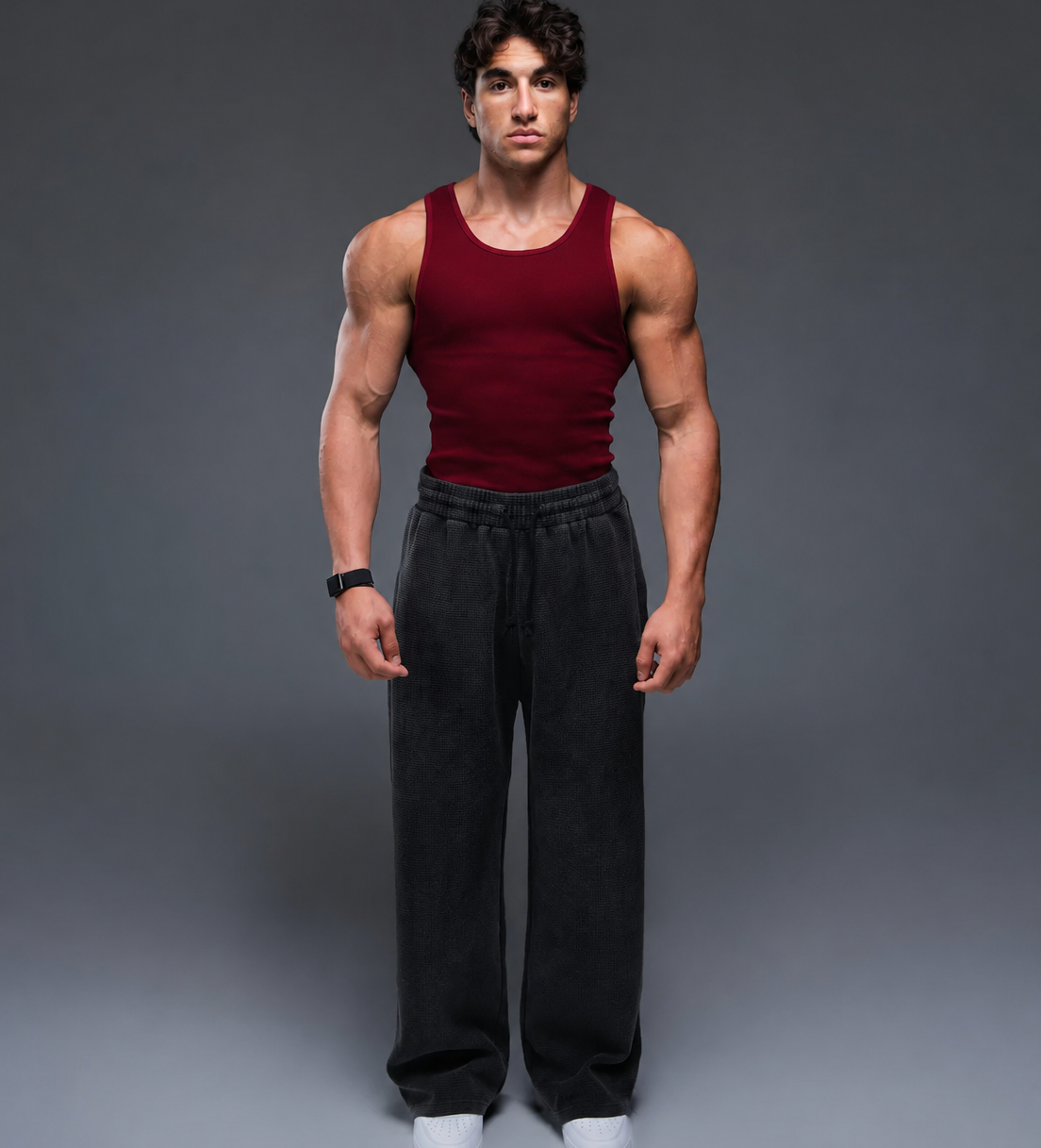Man wearing a red tank top and black pants against a gray background