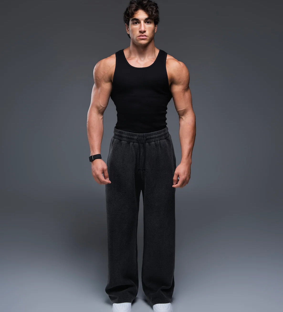Man wearing a black tank top and black pants on a gray background