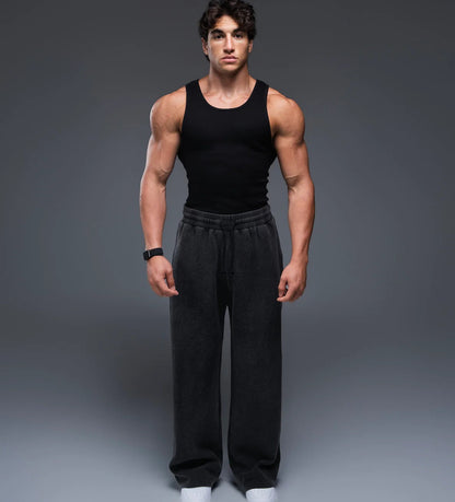 Man wearing a black tank top and black pants on a gray background