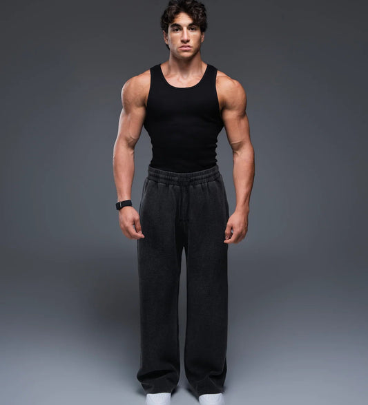 Man wearing a black tank top and black pants on a gray background
